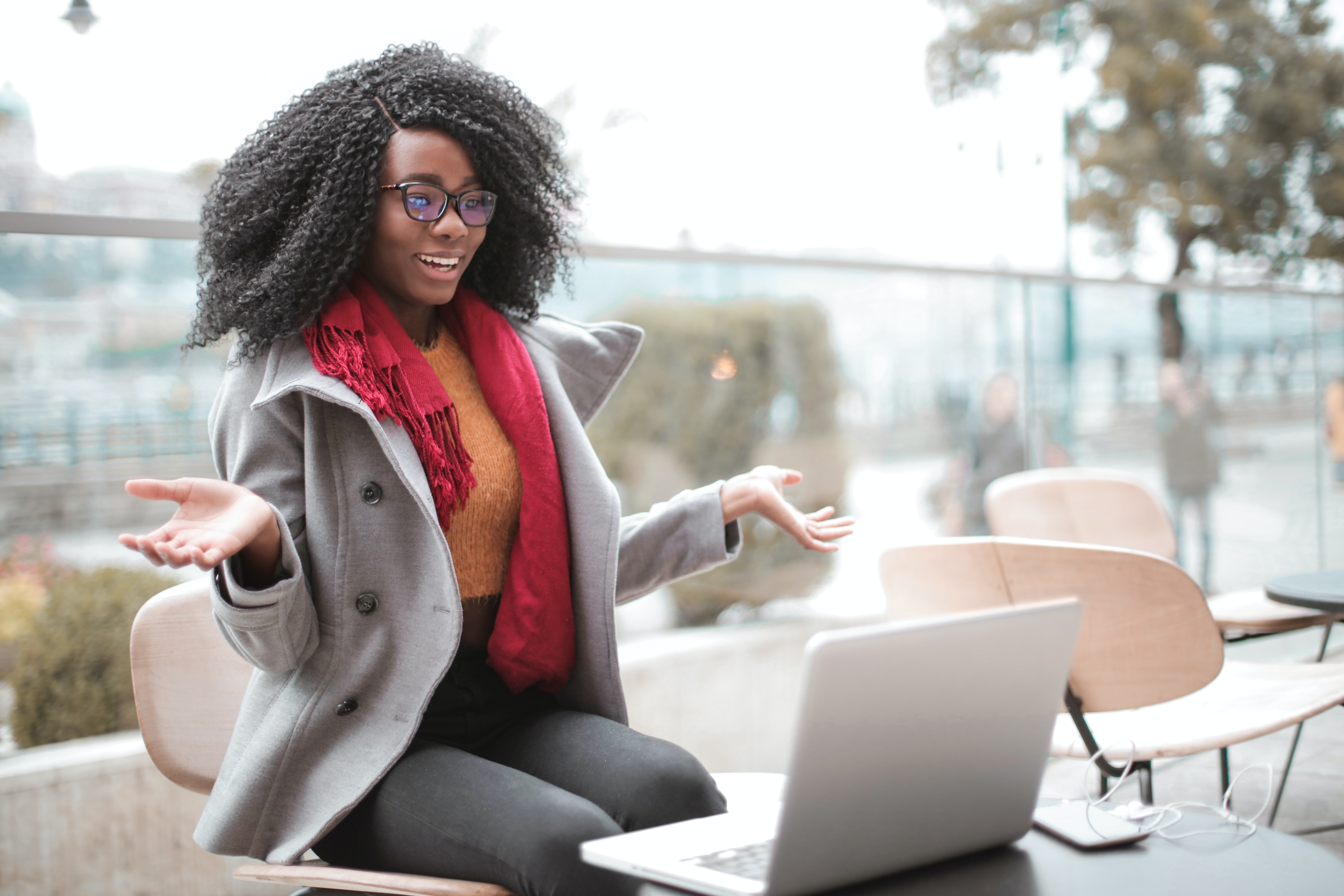 A woman wearing a gray jacket sitting in front of a computer with her arms out 