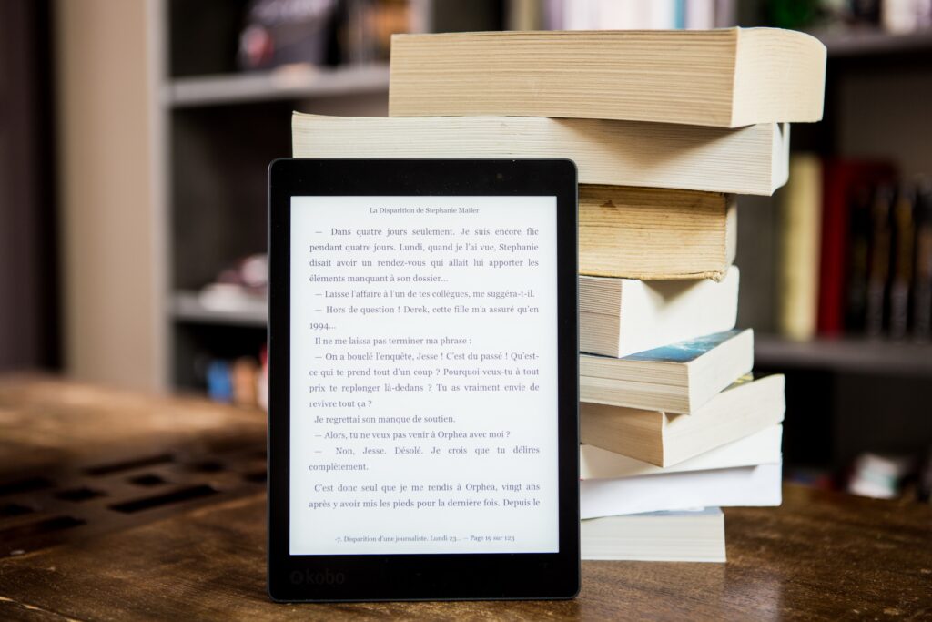 An eBook reader leaning against a stack of paper books