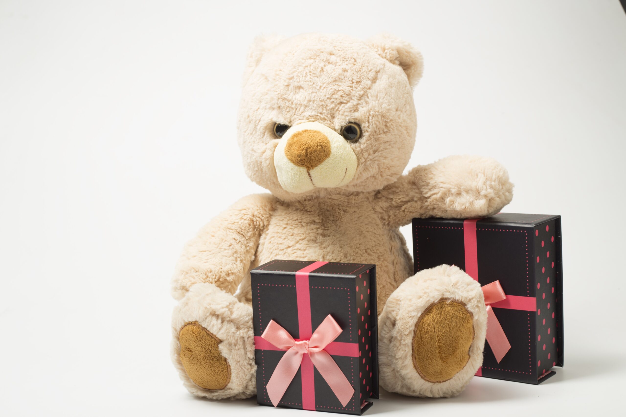 A sassy tan teddy bear sitting with two small wrapped gifts